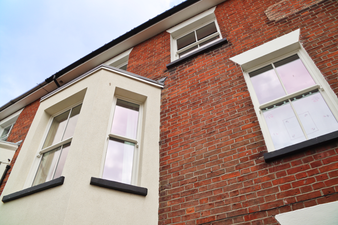 view looking upwards at front of a Victorian town house. Sliding sash bay window and single sliding sash windows painted white. Traditional red brick facade