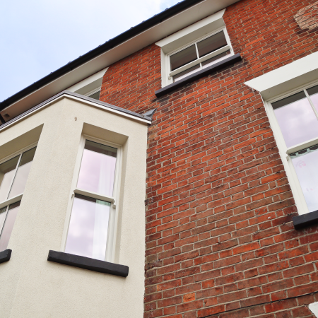 view looking upwards at front of a Victorian town house. Sliding sash bay window and single sliding sash windows painted white. Traditional red brick facade